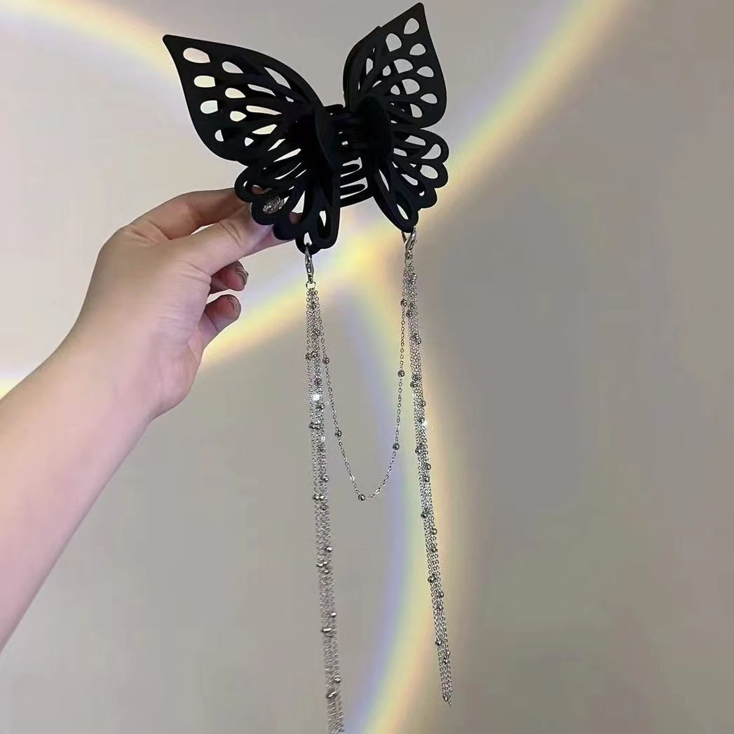 Black butterfly hair accessory with beaded chain held by a hand against a neutral background