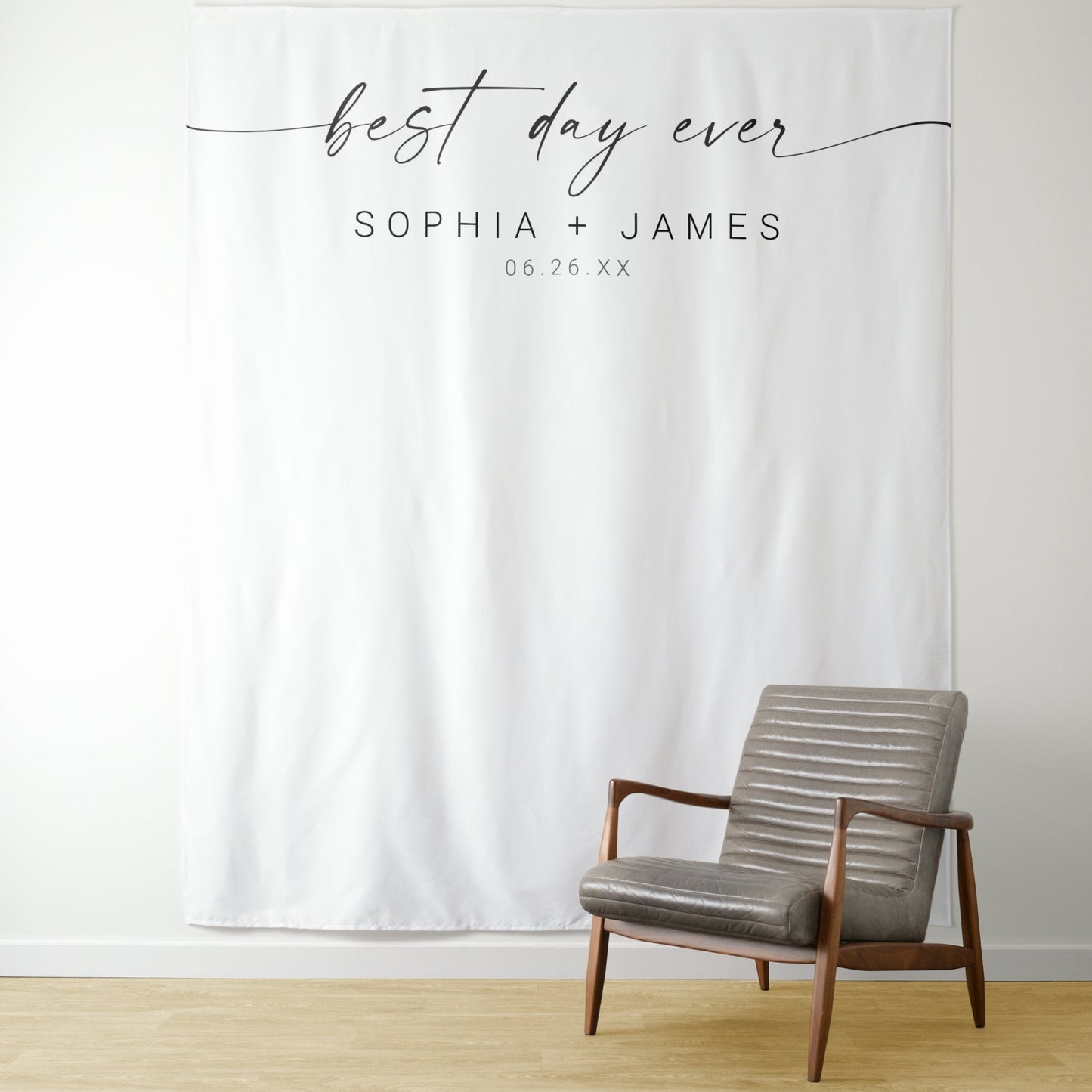 A white polyester wedding backdrop with the text 'Best Day Ever' and names 'Sophia + James' printed on it, displayed in a room with a wooden chair and a white floor.