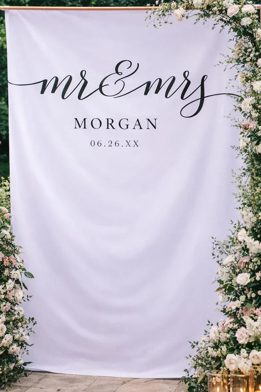 Wedding backdrop with 'mr & mrs' and 'Morgan' text, surrounded by floral decorations and candles.