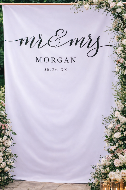 Wedding backdrop with 'mr & mrs' and 'Morgan' text, surrounded by floral decorations and candles.